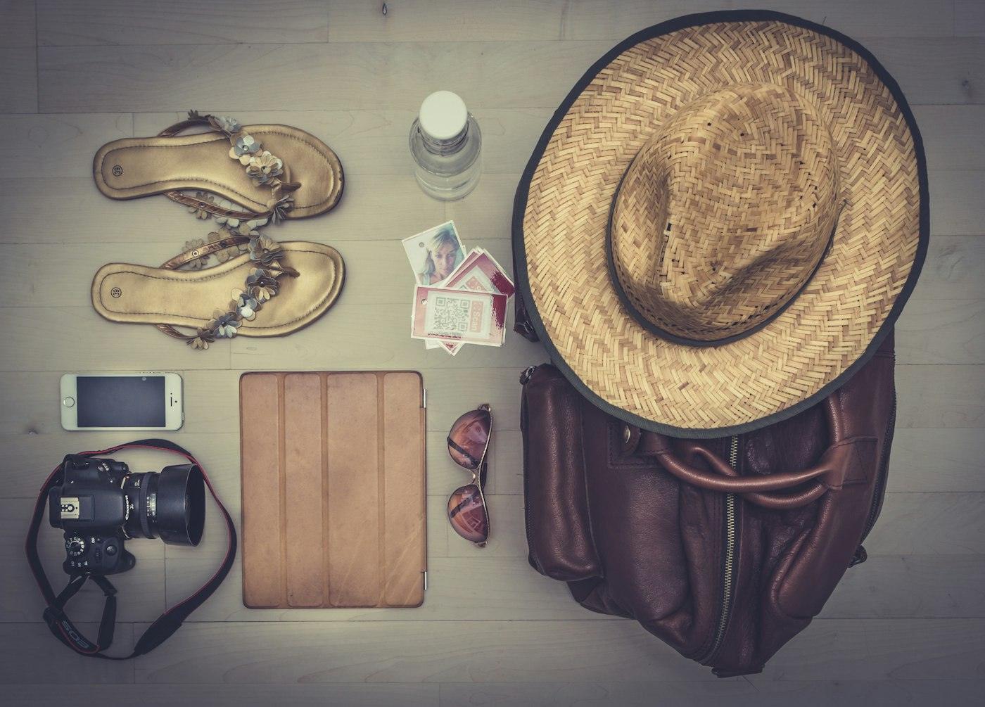 A packing flat lay with camera, hat, and travel essentials